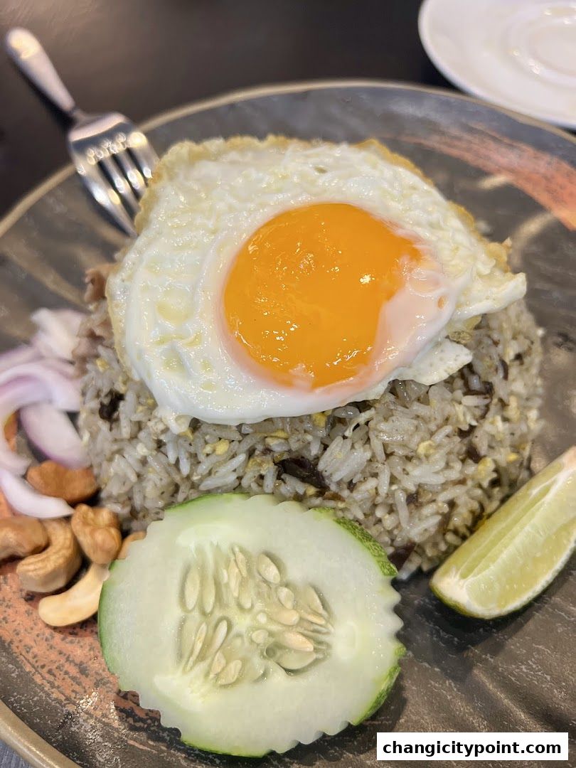 A plate of fried rice topped with a sunny-side-up egg, served with cucumber, lime, and cashews.