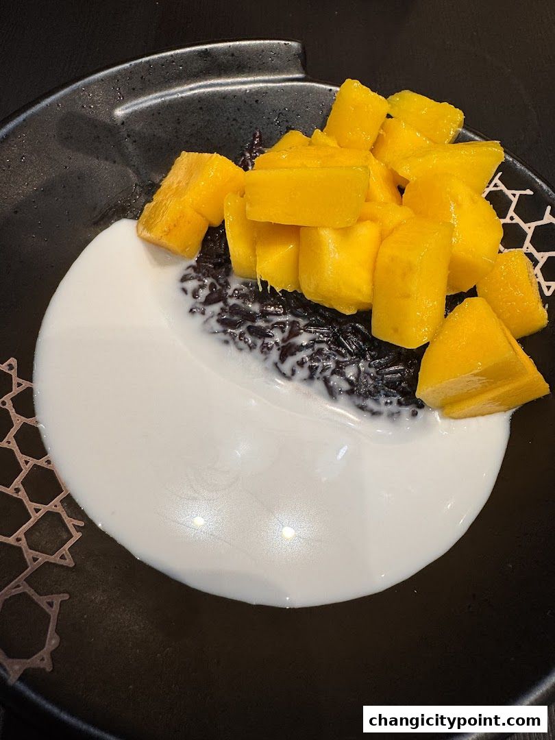 A black bowl filled with black rice pudding, topped with fresh mango cubes and coconut milk.