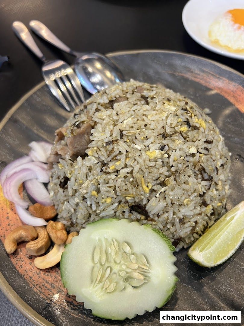 A close-up of a plate of fried rice with meat, garnished with cucumber, lime, cashews, and onion.