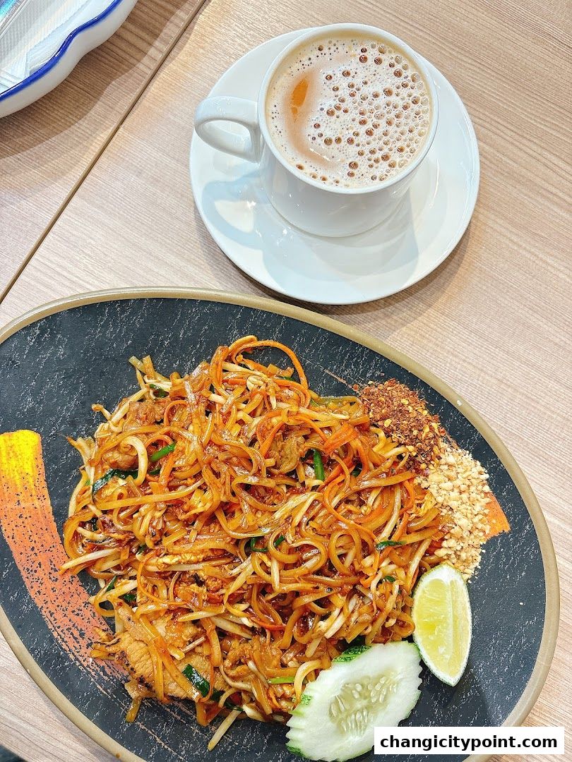 A plate of Pad Thai noodles with a side of lime and cucumber, and a cup of coffee.