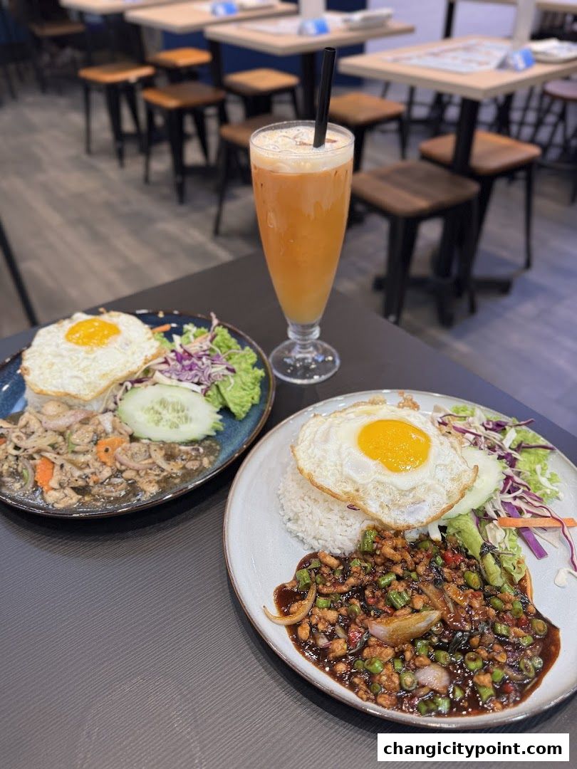 Two plates of Thai food with fried eggs and a Thai iced tea on a table.