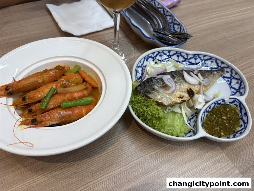 A close-up of two Thai dishes: a bowl of prawns and a grilled fish with salad.