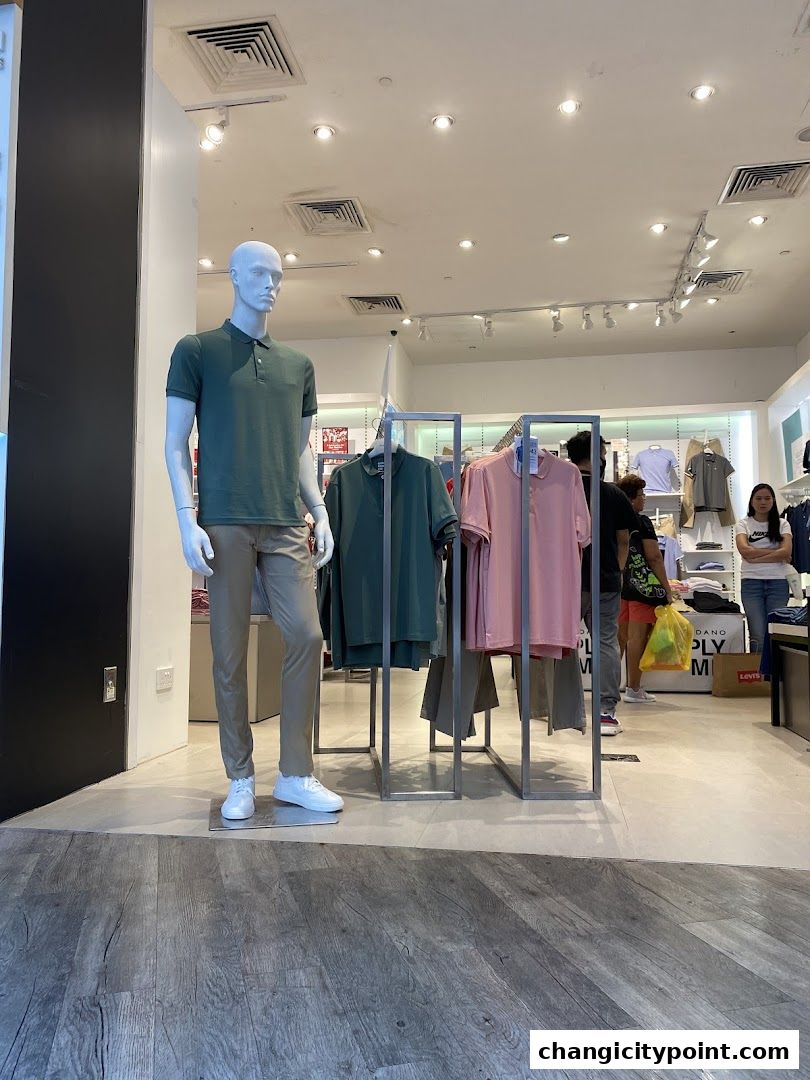 Mannequin in a green polo shirt and tan pants, with clothing displays inside a Giordano store.