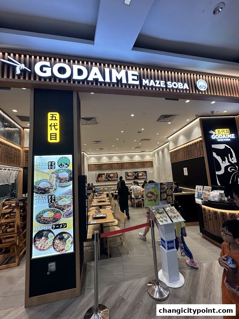 The entrance of Godaime Maze Soba restaurant with a menu display and seating visible inside.