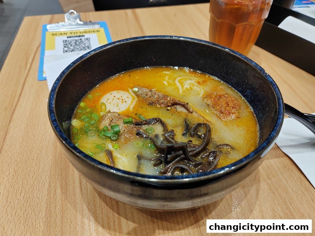 A steaming bowl of ramen with various toppings and a glass of iced tea.