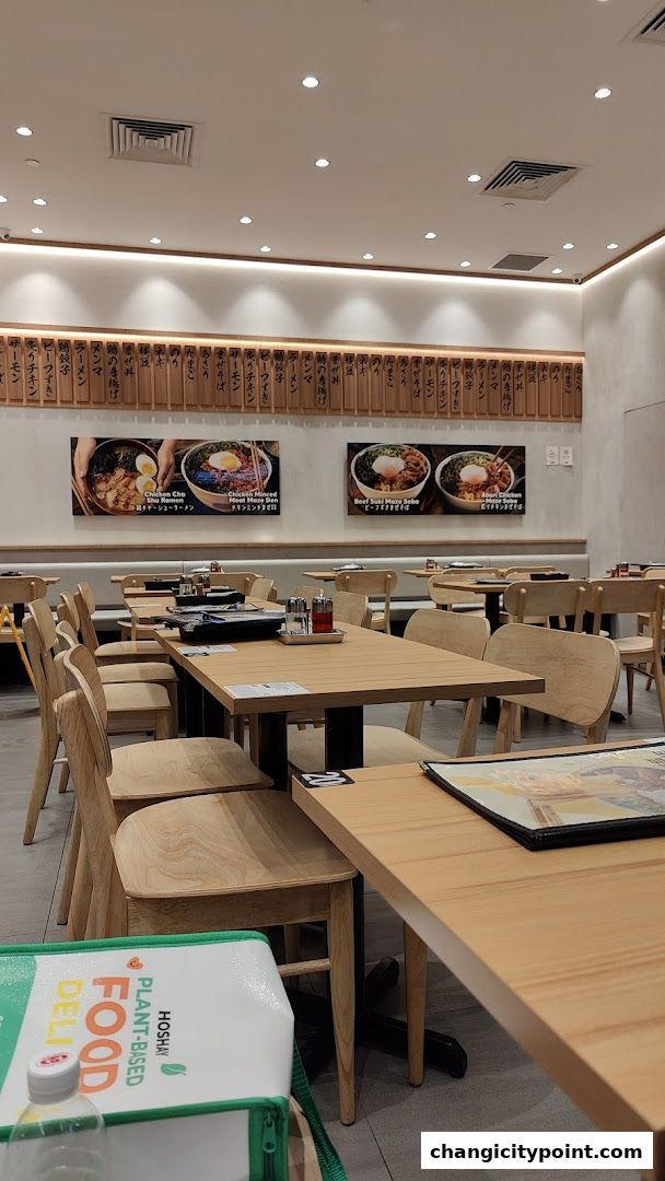 Interior of a Japanese restaurant with wooden tables and chairs, and food images on the wall.