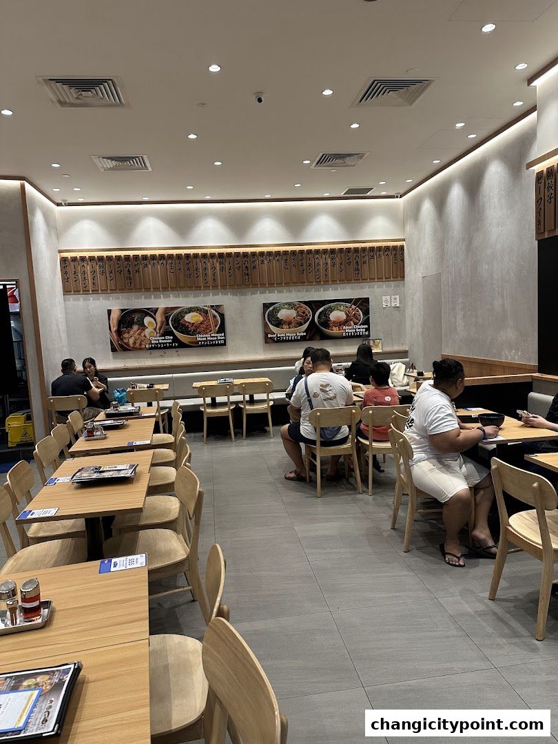 Interior of a Japanese restaurant with diners seated at tables and food images on the wall.