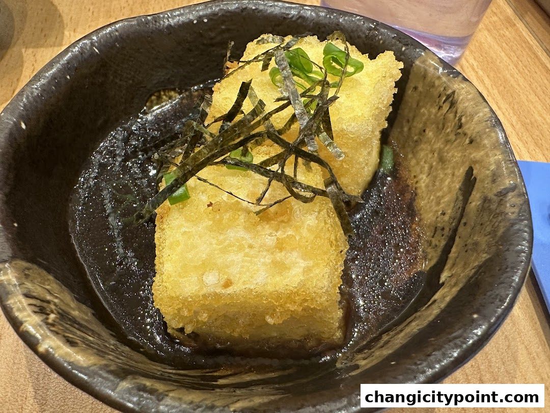Crispy fried tofu served in a dark bowl with sauce and seaweed.