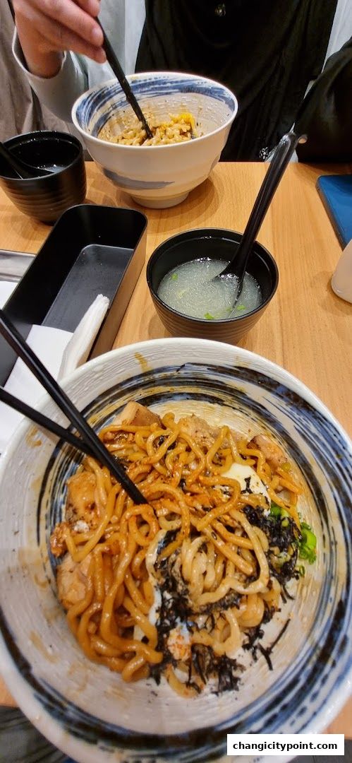 Close-up of two bowls of noodles and rice dishes with chopsticks and soup.
