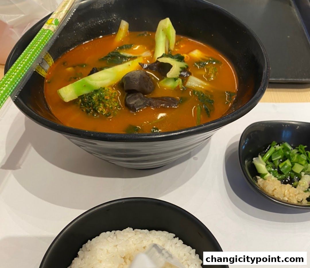A bowl of Mala Tang soup with vegetables and a side of rice.