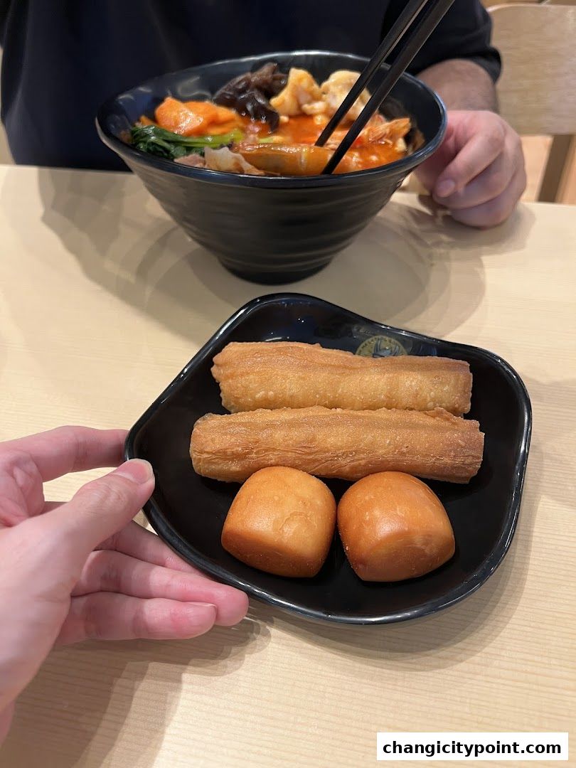 A bowl of Mala Tang with fried dough sticks and steamed buns on a plate.