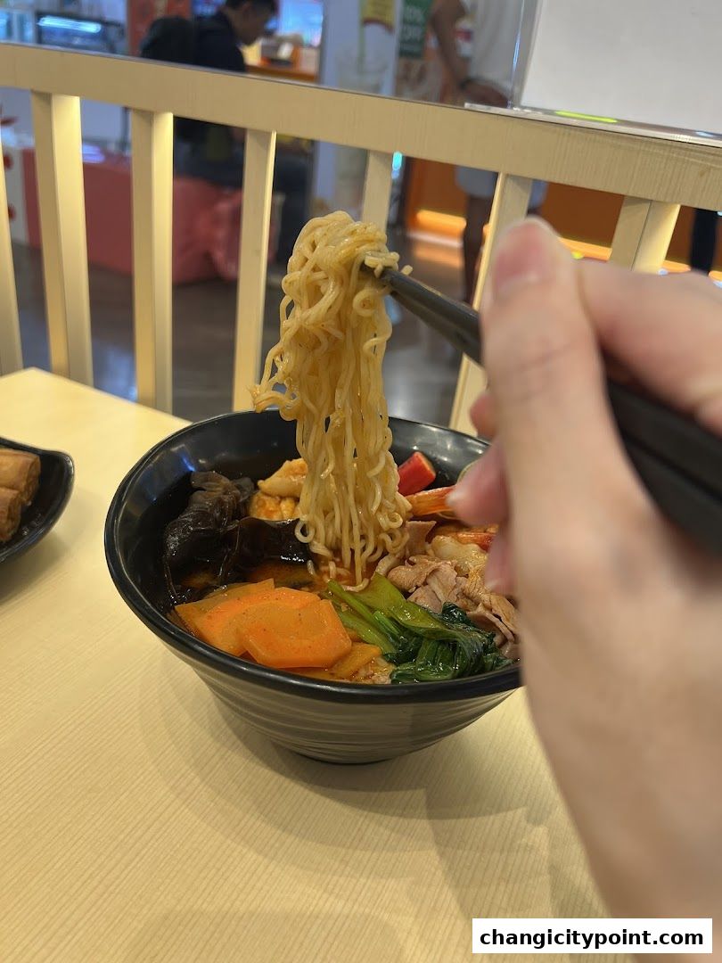 A hand uses chopsticks to lift noodles from a bowl of Mala Tang.