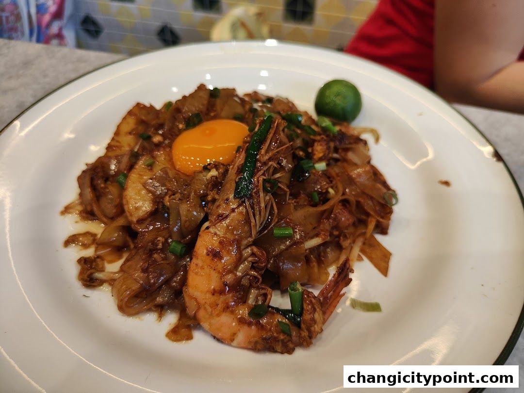 A plate of delicious-looking Char Kway Teow with prawns and a runny egg yolk.