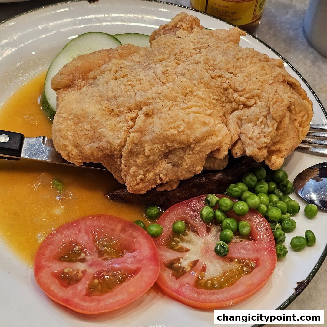 A close-up of a crispy fried chicken dish with peas, tomatoes, and cucumber slices.