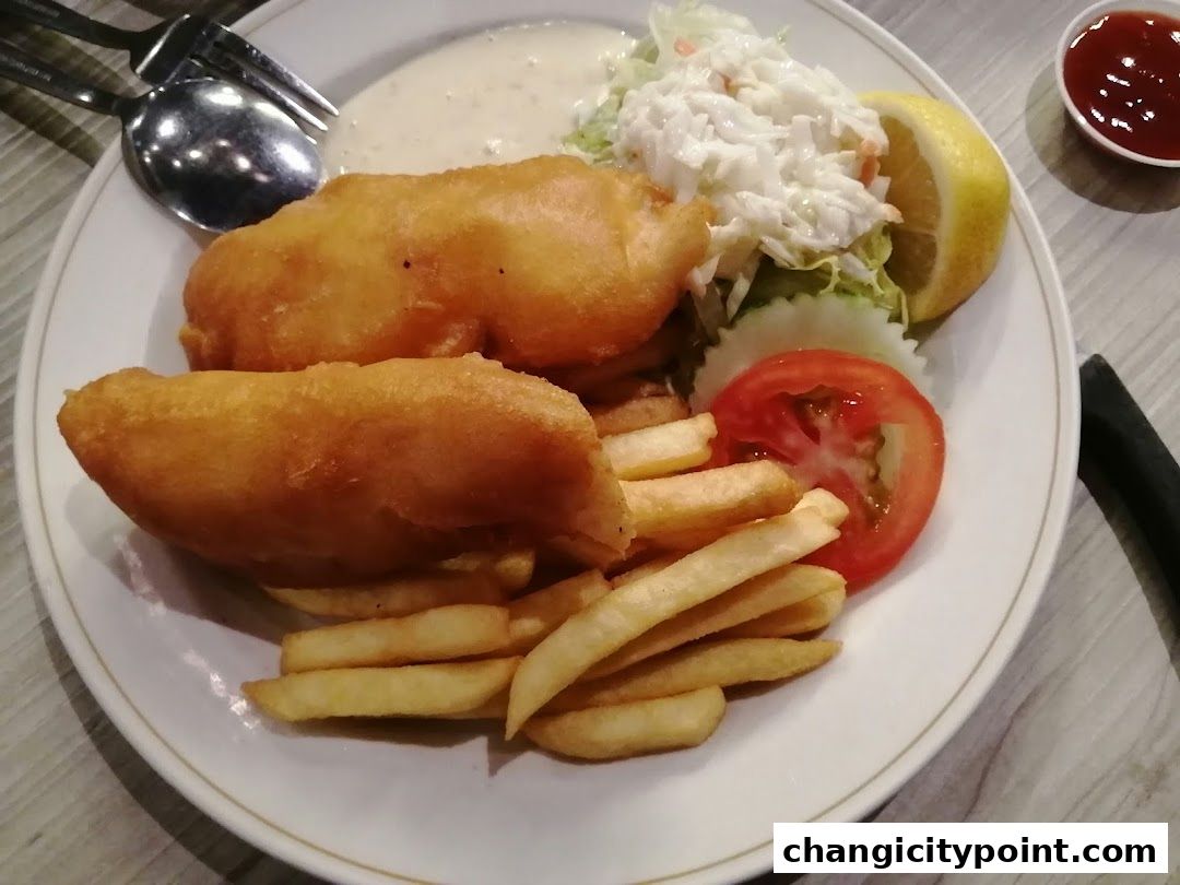 A plate of fish and chips with coleslaw, lemon, and a side of ketchup.