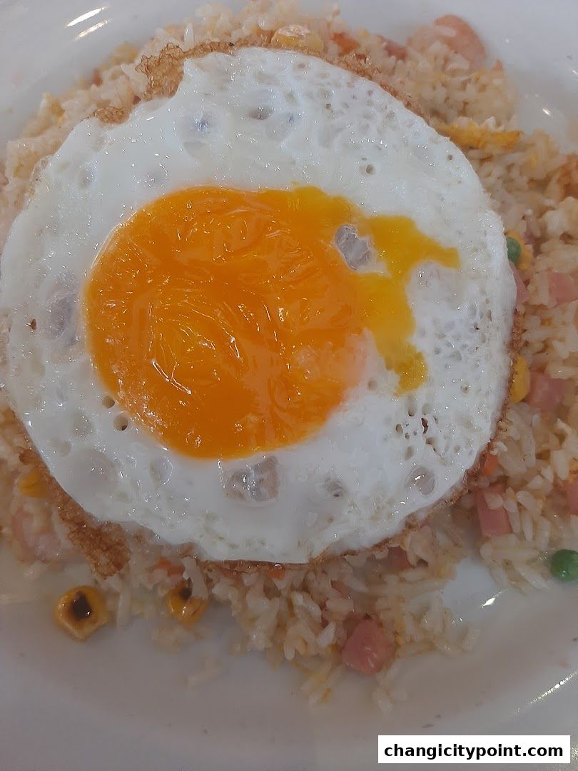 A close-up of fried rice topped with a sunny-side-up egg and mixed with corn and ham.