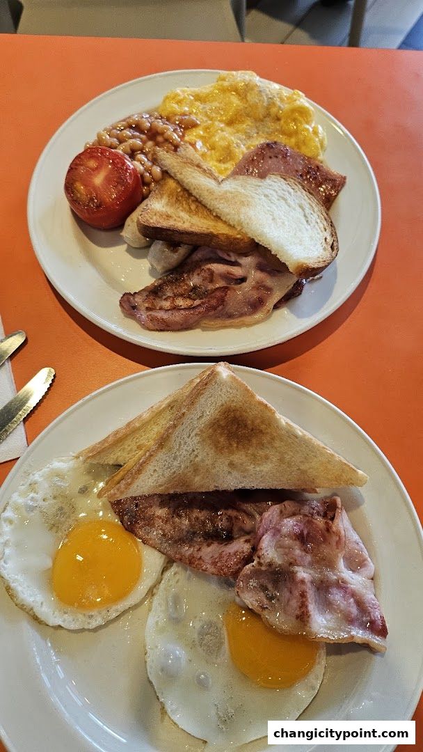 Two plates of hearty breakfast with eggs, bacon, beans, tomato, and toast.