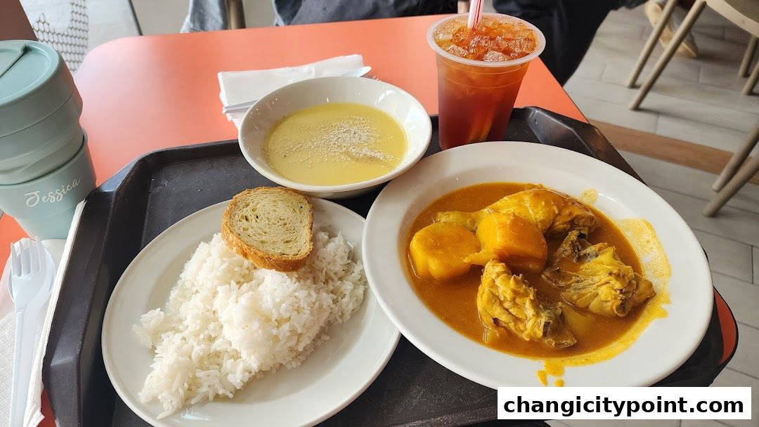 A tray of food from Hans Cafe Changi City Point, featuring curry chicken, rice, soup, and iced tea.