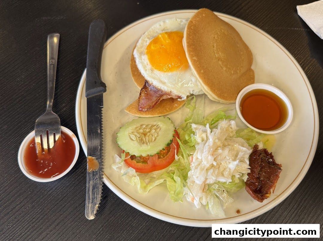 A plate of pancakes with a fried egg, bacon, salad, and syrup, served with ketchup.