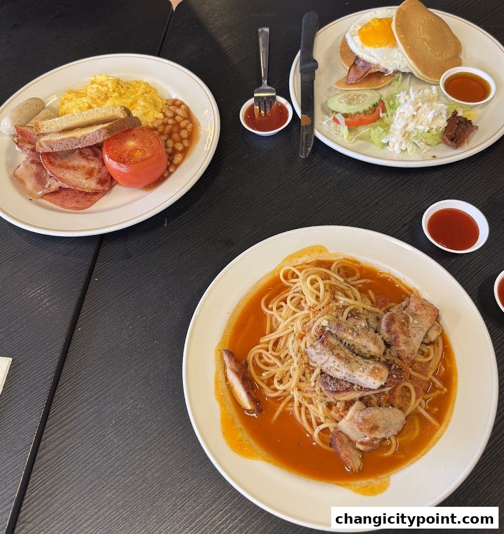 Three plates of food, including a full breakfast, pancakes, and pasta, are laid out on a dark table.
