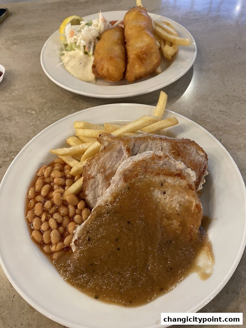 Two plates of food, one with fish and chips, the other with pork chops and beans.