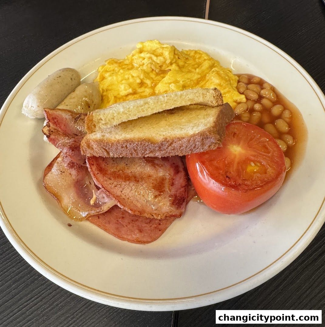 A hearty breakfast plate with scrambled eggs, bacon, sausages, toast, beans, and tomato.