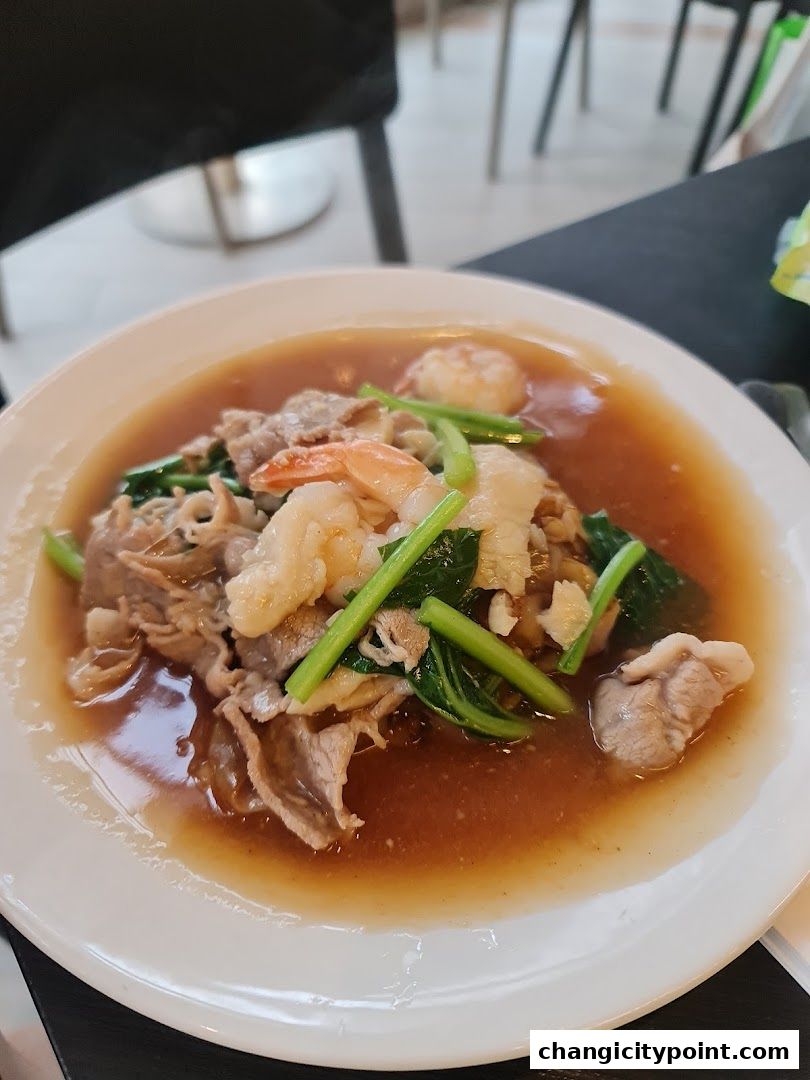 A close-up of a delicious noodle dish with beef, shrimp, and vegetables in a savory sauce.