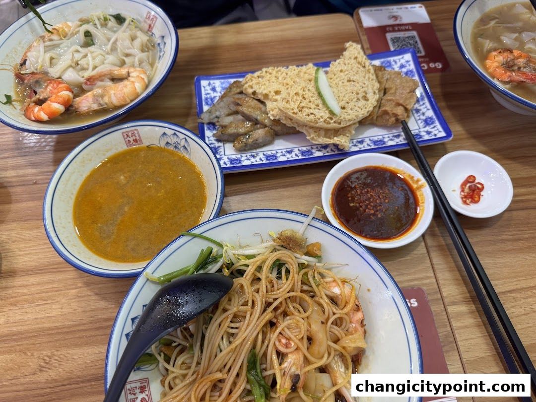 A table laden with delicious prawn noodle dishes and various side items.