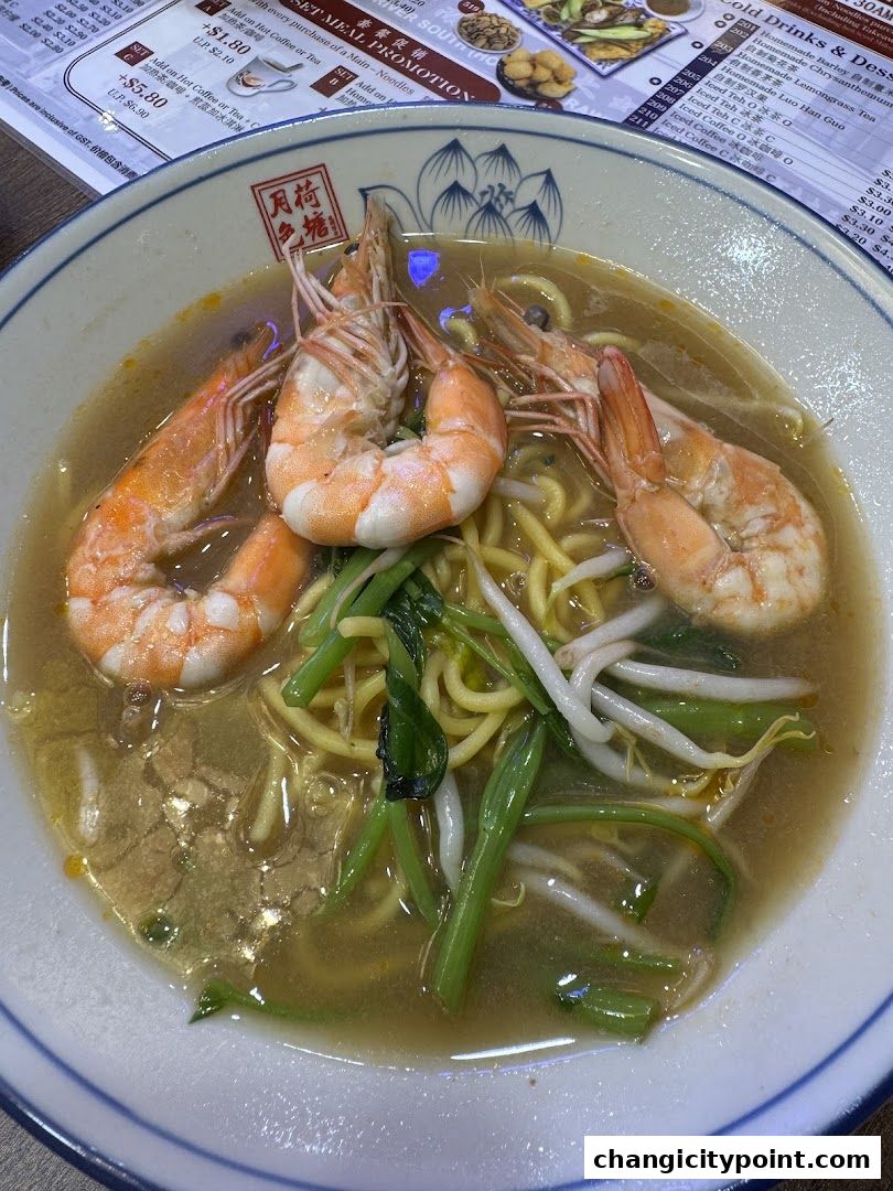 A close-up of a bowl of prawn noodles with large prawns, noodles, and vegetables.