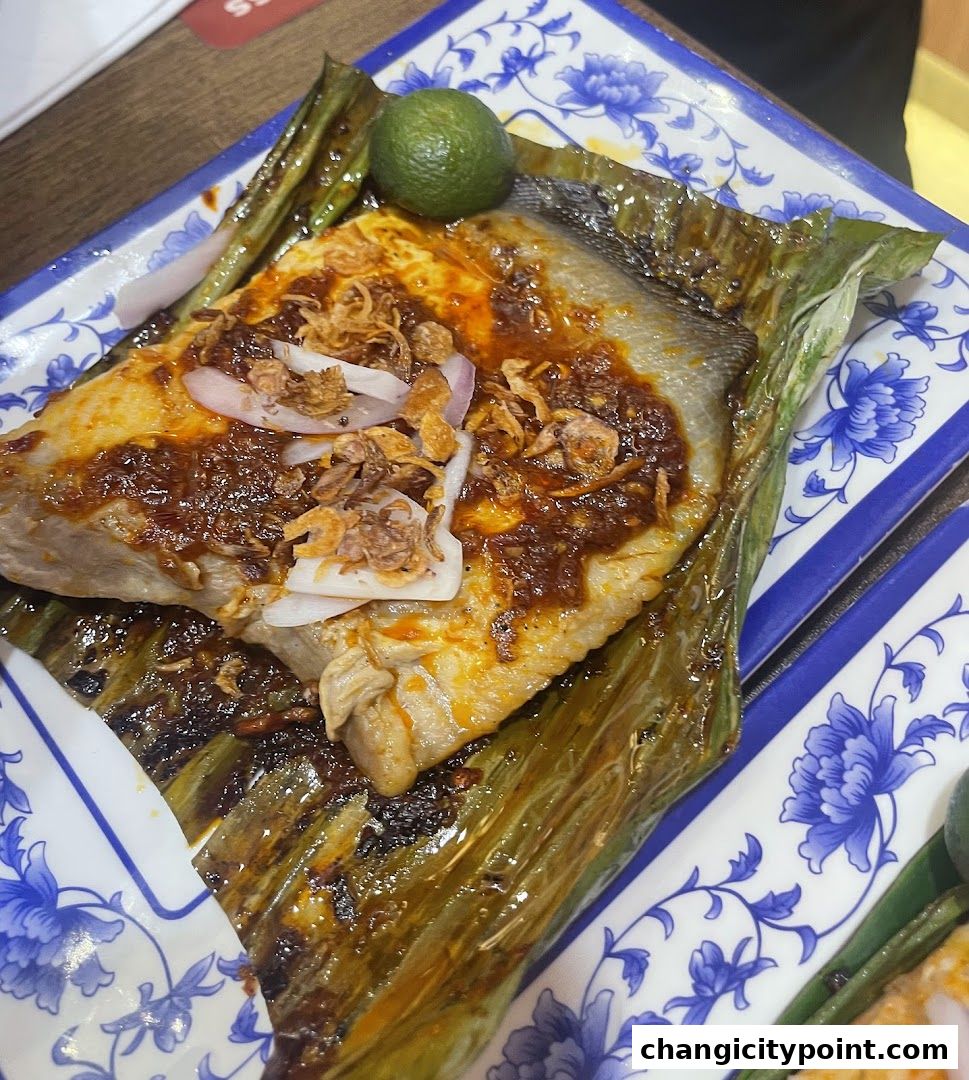 A close-up of a delicious fish dish wrapped in banana leaves, topped with chili paste and fried shallots.