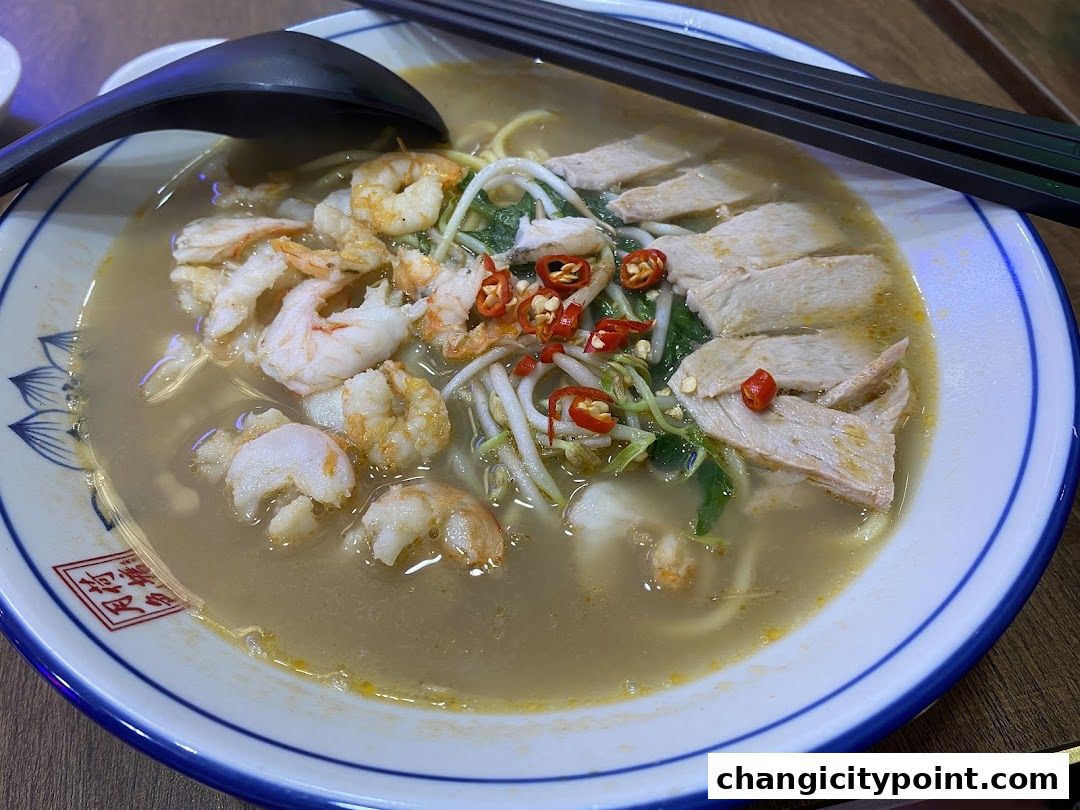 A close-up of a delicious bowl of prawn noodles with shrimp, meat, and chili.