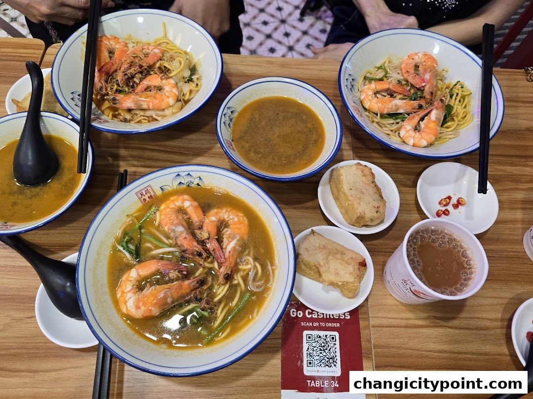 Bowls of prawn noodles and side dishes served on a wooden table.