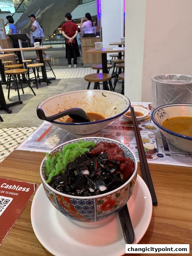A close-up of a dessert with green jelly, black jelly, and red beans, served in a decorative bowl.