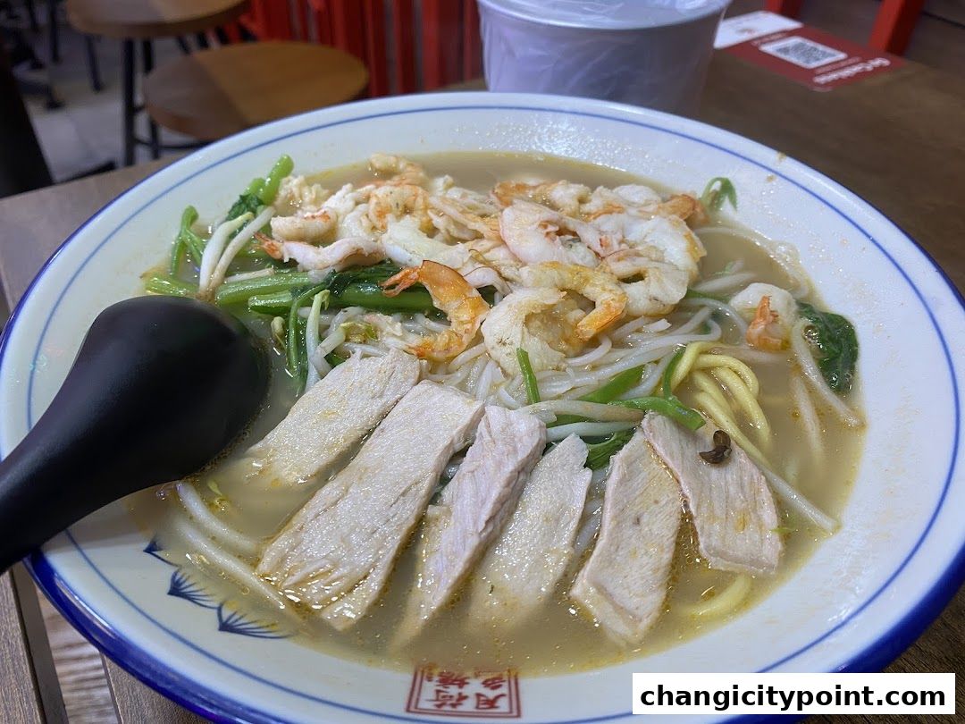 A close-up of a bowl of prawn noodles with sliced chicken and vegetables.