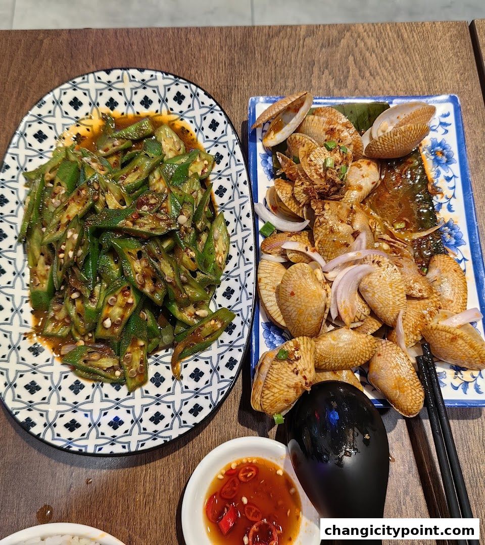 A plate of stir-fried okra and a dish of clams with onions and chili sauce.