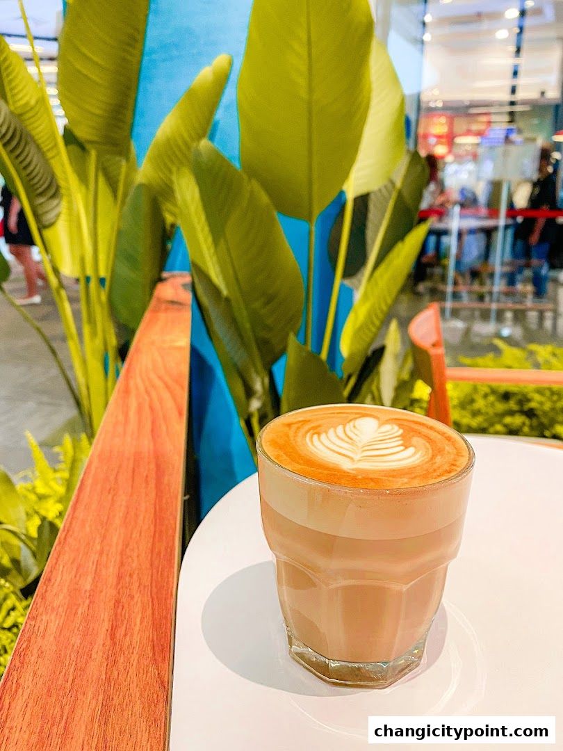 A glass of latte with latte art on a white table, with plants in the background.
