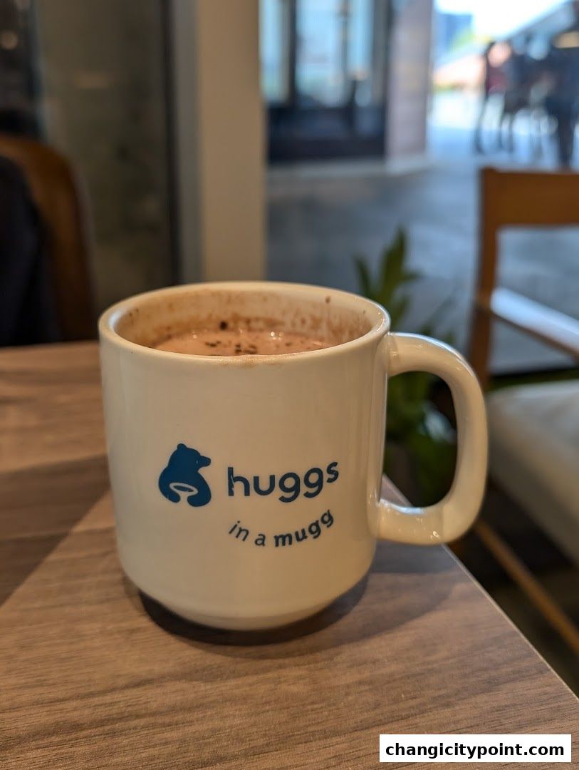 A white mug with the Huggs Coffee logo and slogan sits on a wooden table.