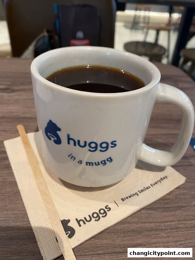 A white mug of black coffee sits on a napkin with a wooden stirrer.