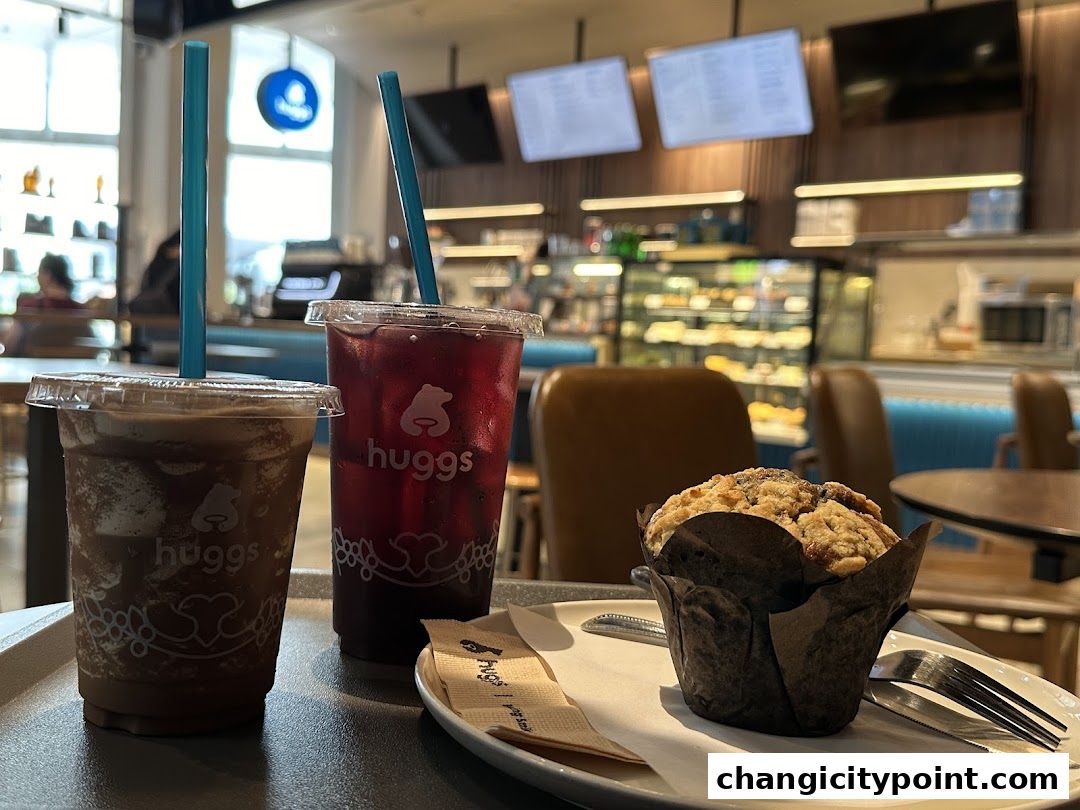 Two drinks and a muffin on a tray at Huggs Coffee, with a display case and seating in the background.