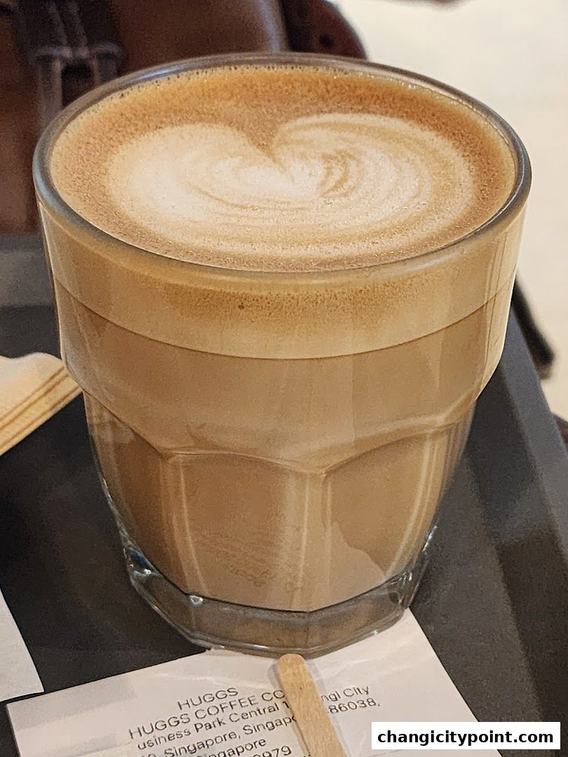 A close-up of a latte with heart-shaped foam art in a clear glass.