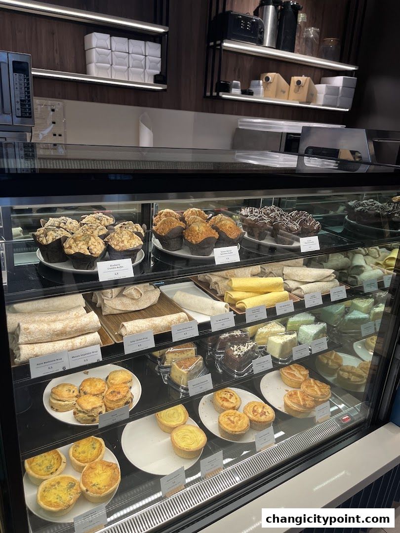 A display case filled with various pastries, muffins, wraps, quiches, and cakes at Huggs Coffee.