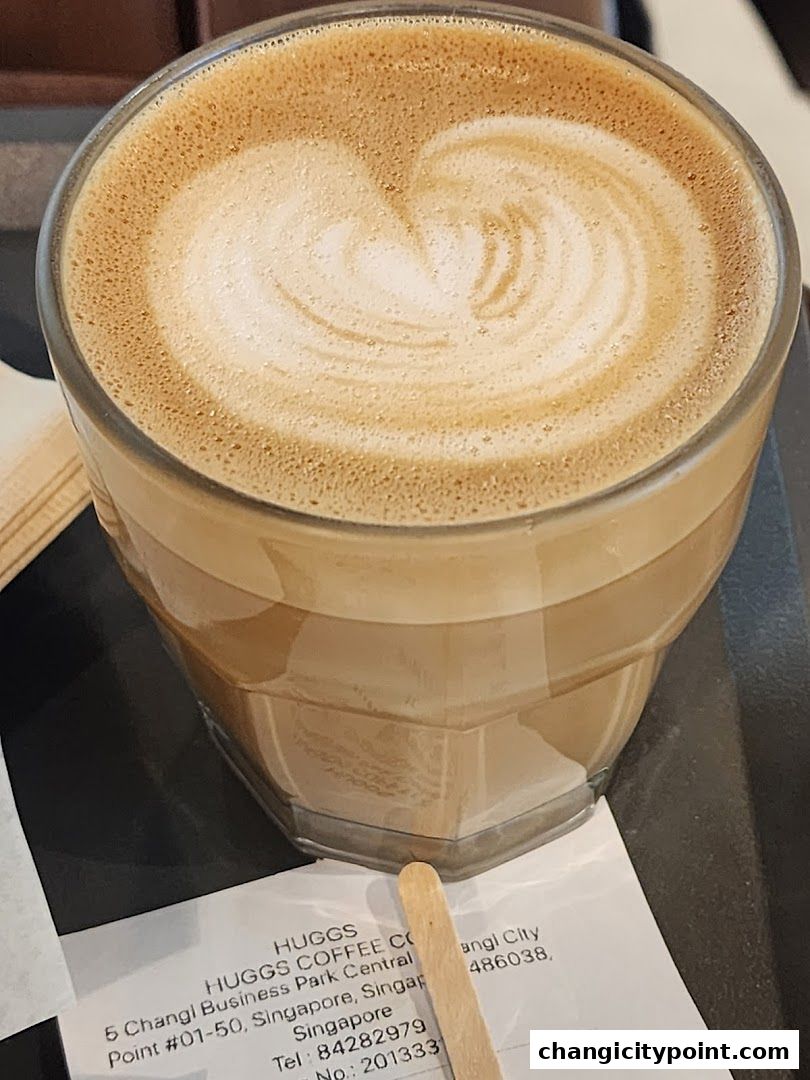 A close-up of a latte with heart art, served in a glass, with a receipt from Huggs Coffee.