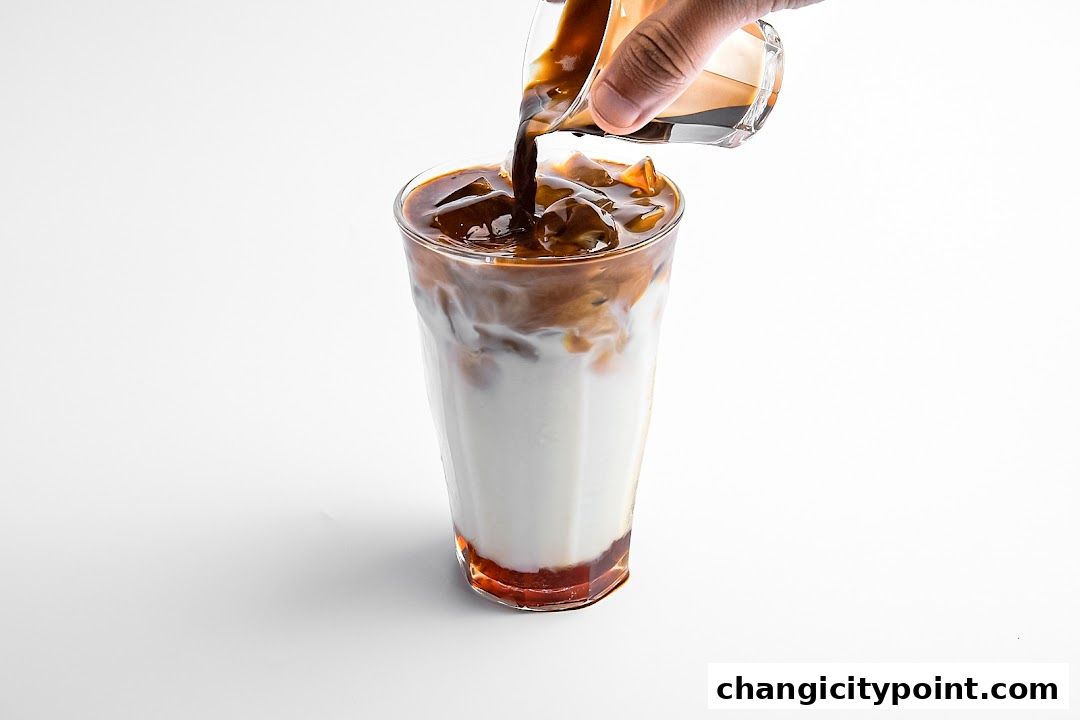 A hand pours dark coffee into a tall glass of milk and ice.