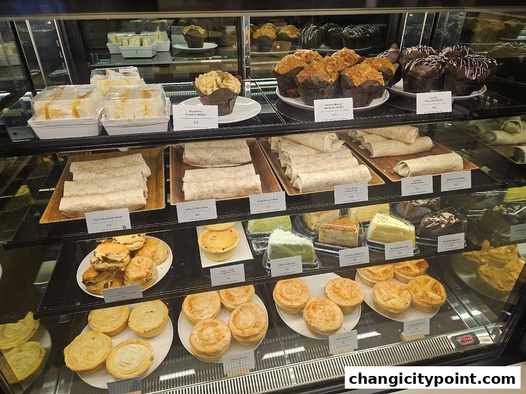 A display case filled with various pastries, sandwiches, wraps, and cakes.