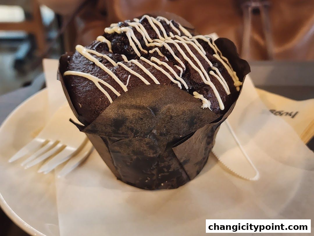 A close-up of a decadent chocolate muffin with white icing drizzle.