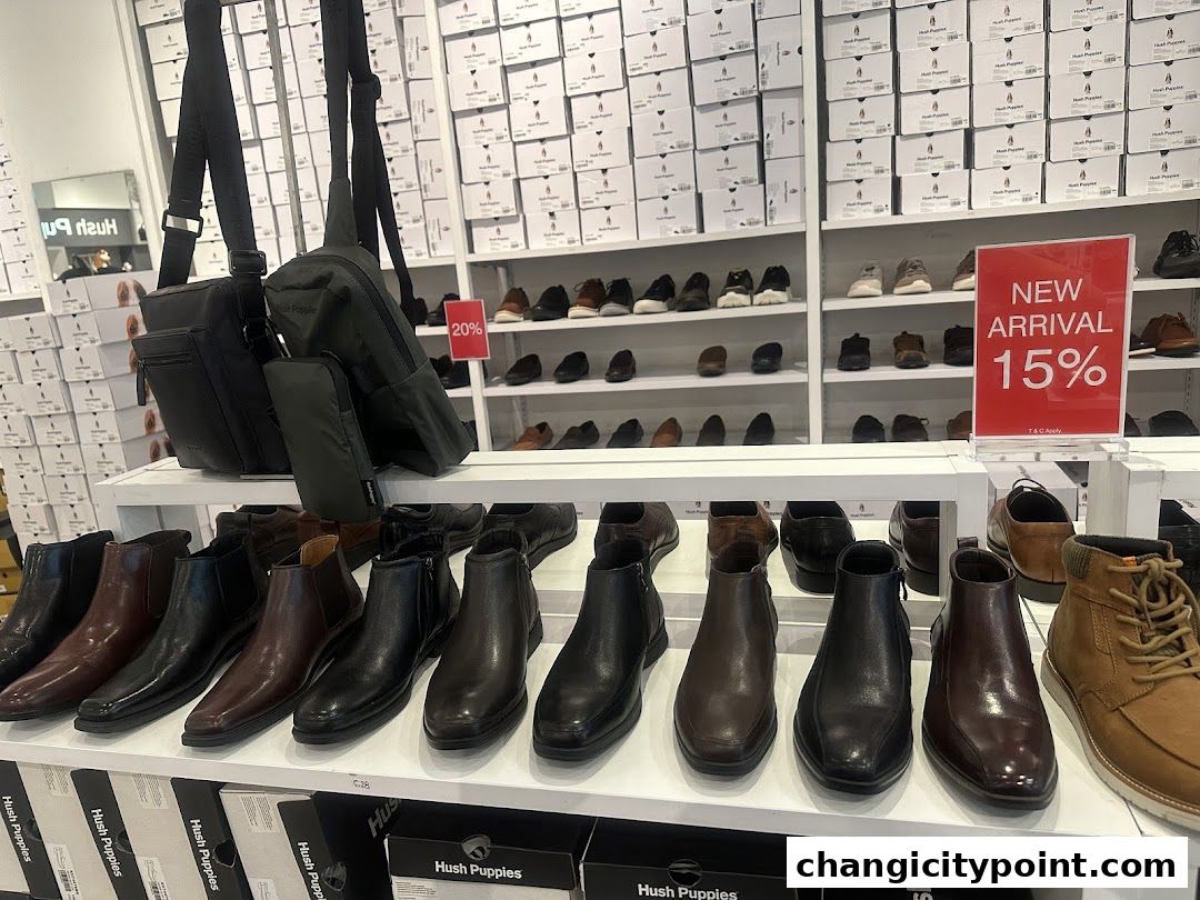 A retail store interior displaying rows of Hush Puppies shoes and bags, with a 'New Arrival 15%' sign.