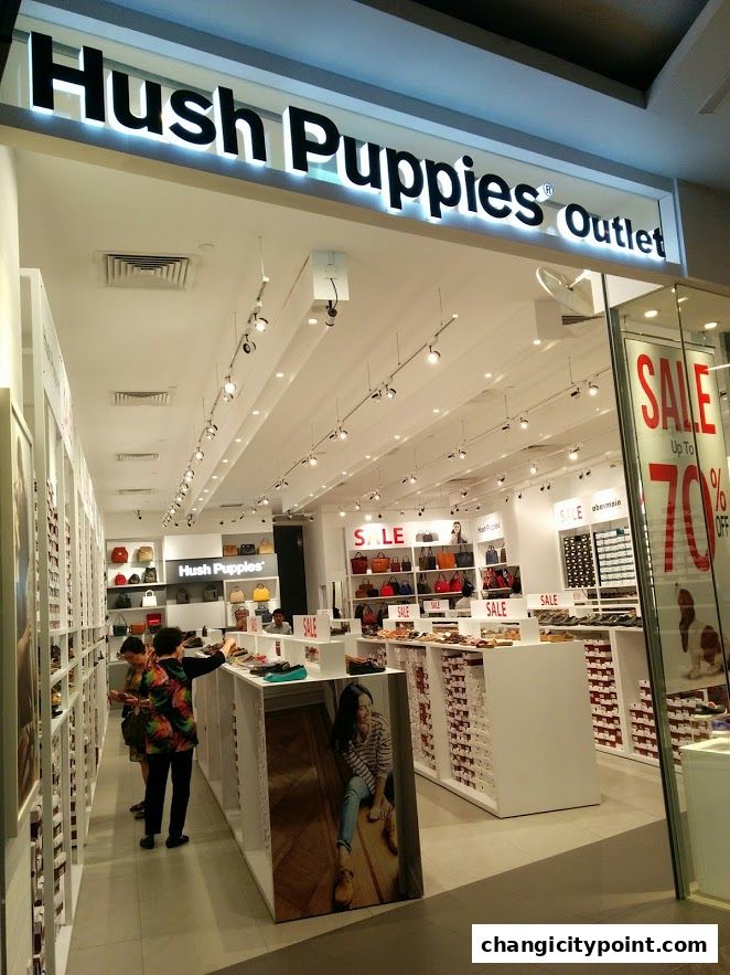 The entrance of a Hush Puppies Outlet store with shoes and bags on display, featuring a sale.