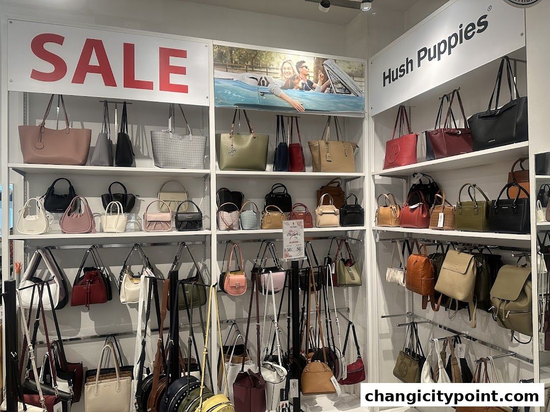 A wide selection of Hush Puppies handbags displayed on shelves with a prominent 'SALE' sign.