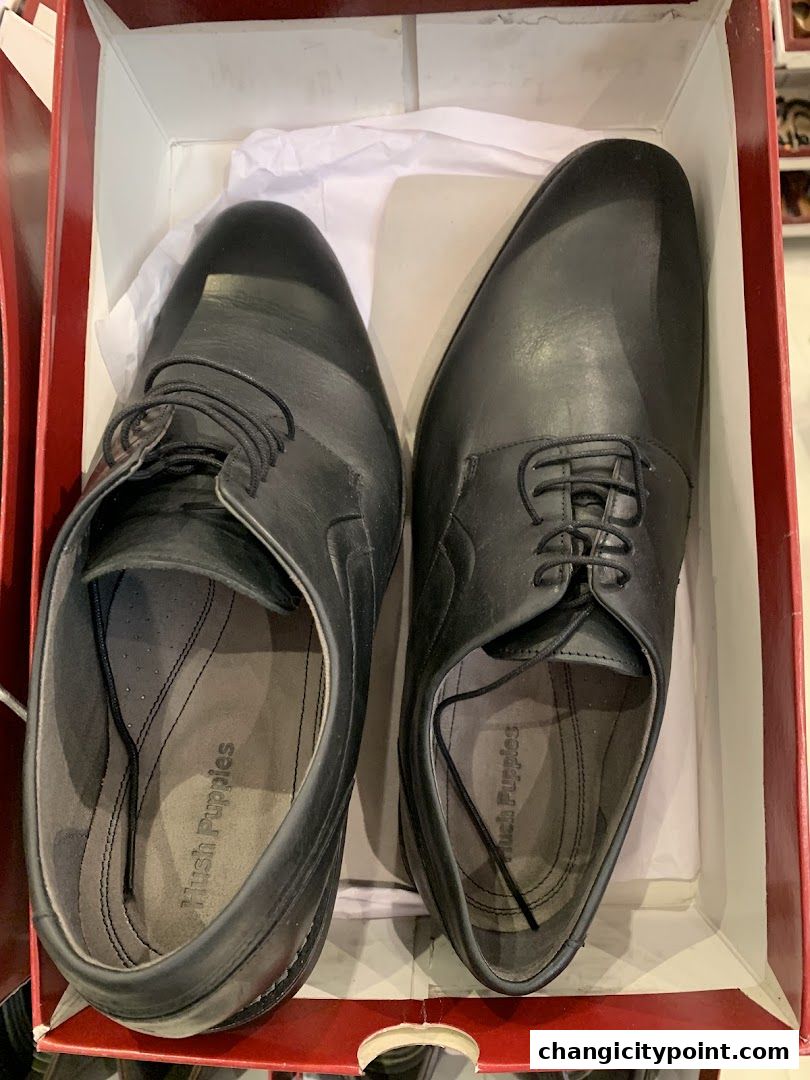 A pair of black Hush Puppies dress shoes in a red and white box.