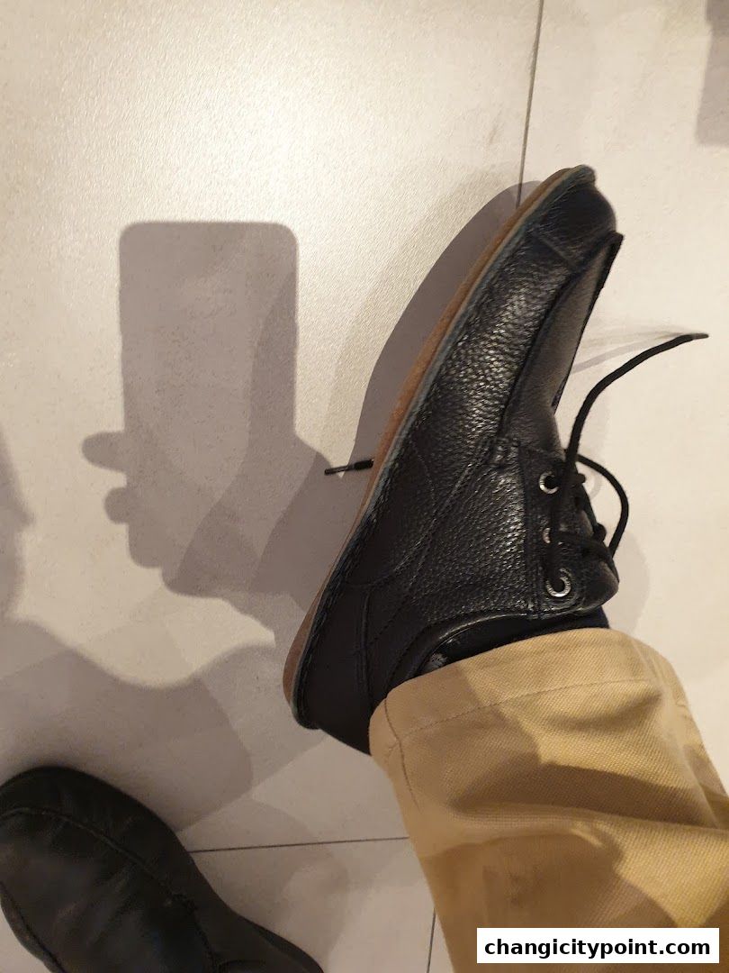 A close-up shot of a person wearing black Hush Puppies shoes and tan pants.